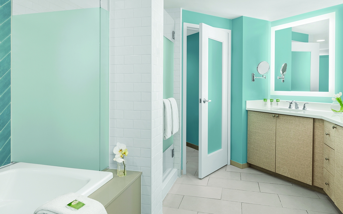 Villa master bathroom with oversized tub. Teal and white color palette, walk-in shower, lighted double-vanity.