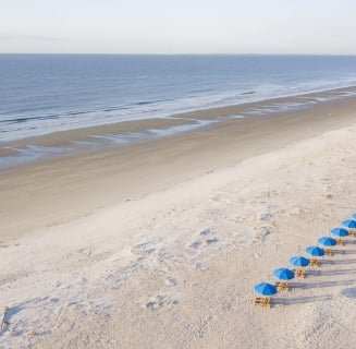 chairs with blue umbrellas lined up on a white sand beach
