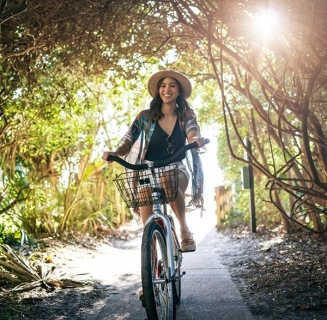 woman in floral top and hat on a bike under a covered bike path with sun poking through at Palmetto Dunes Oceanfront Resort