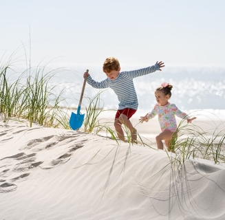 Little boy with shovel and little girl climb the sand dunes at the beach at Palmetto Dunes