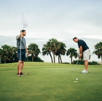 two men putting on green with palm trees in background