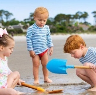 three children with shovels digging on the beach