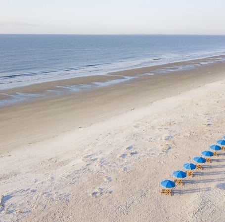 chairs with blue umbrellas lined up on a white sand beach