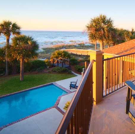 view from the balcony of a vacation home at sunset overlooking a private pool and the ocean