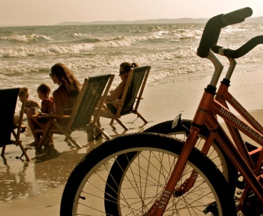 Two bikes parked on a beach with a family in beach chairs in the background