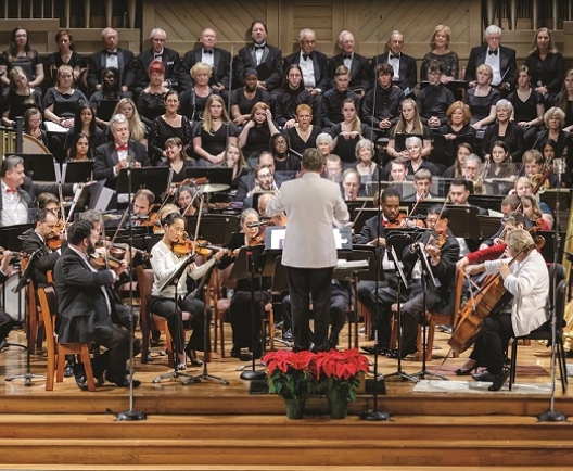 Man in white suit leading a orchestra with many musicians playing instruments