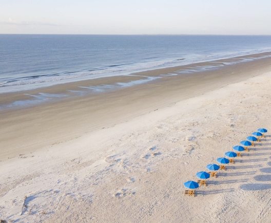 chairs with blue umbrellas lined up on a white sand beach