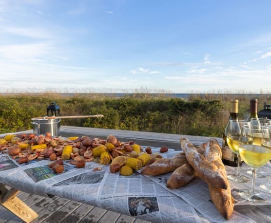 A lowcountry boil set on a large table with white wine and the beach in the distance