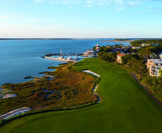 aerial view of golf course with water and lighthouse in the background