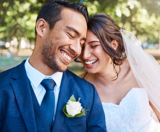 Joyful bride and groom leaning against each other while enjoying romantic moments on wedding day in park on a sunny day