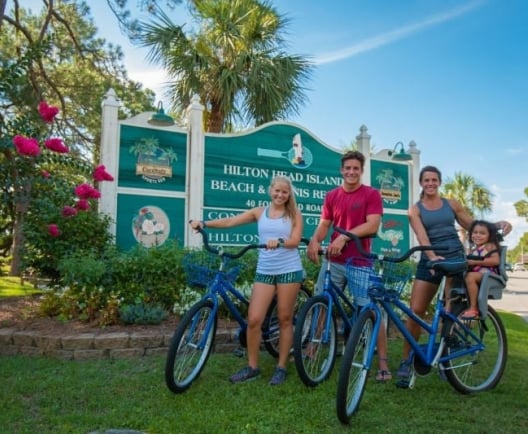 Family of four poses with their bicycles in front of the Hilton Head signage