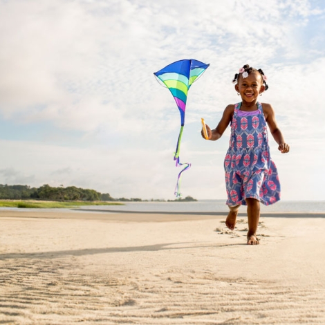 child running on the beach with a kite