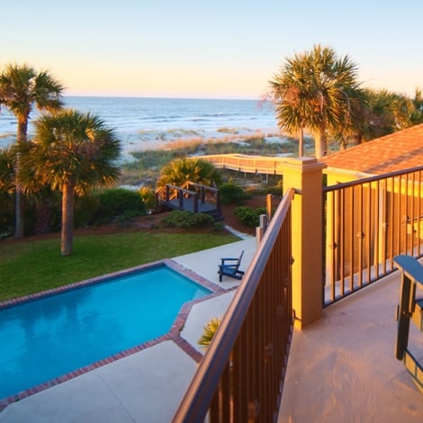 view from the balcony of a vacation home at sunset overlooking a private pool and the ocean