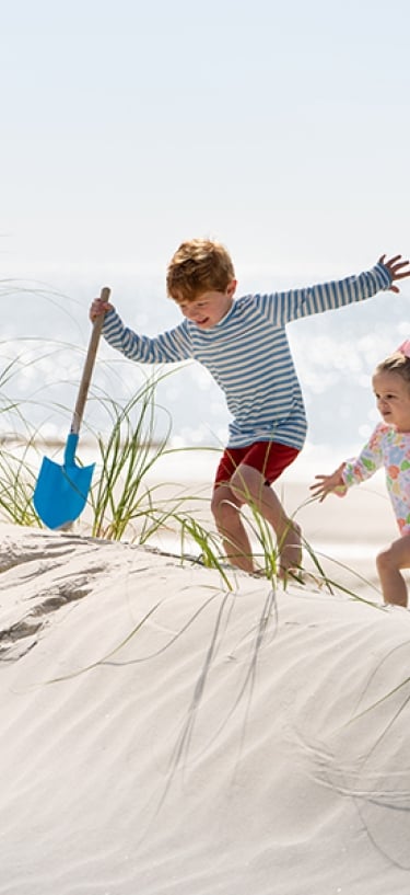 Little boy with shovel and little girl climb the sand dunes at the beach at Palmetto Dunes