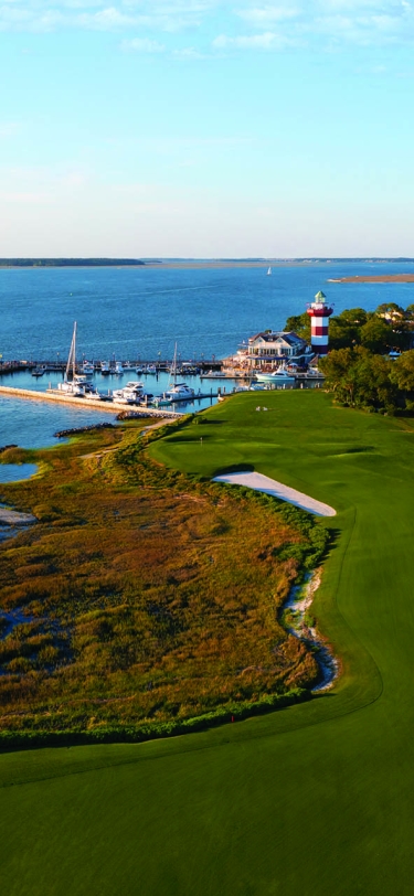 aerial view of golf course with water and lighthouse in the background