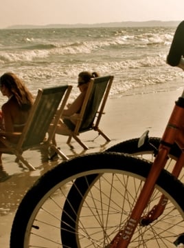 Two bikes parked on a beach with a family in beach chairs in the background