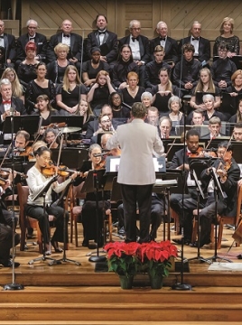 Man in white suit leading a orchestra with many musicians playing instruments