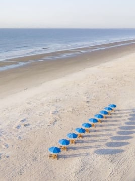 chairs with blue umbrellas lined up on a white sand beach
