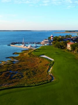 aerial view of golf course with water and lighthouse in the background