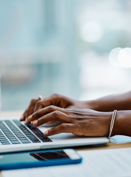 Closeup of a black businesswoman typing on a laptop keyboard in an office alone