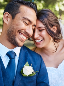 Joyful bride and groom leaning against each other while enjoying romantic moments on wedding day in park on a sunny day