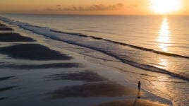 An aerial view of a long beach with a solo walker.