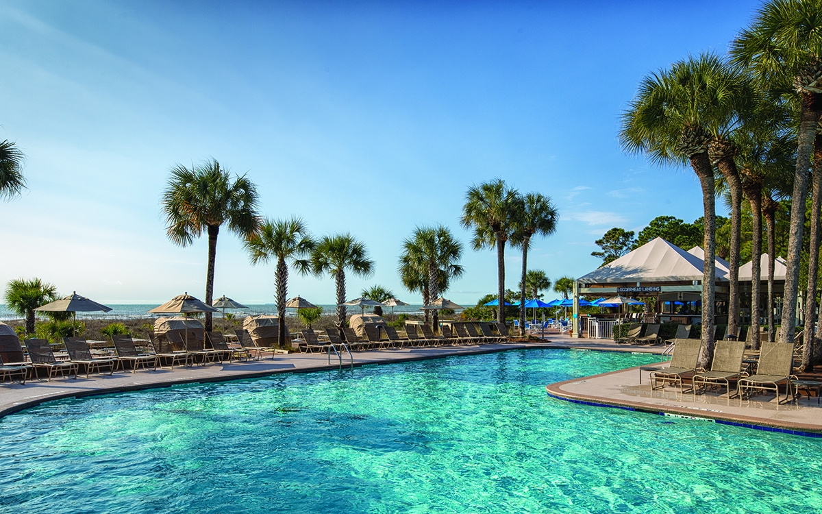 South Pool with pool chairs lined around pool, palm trees, Loggerhead Landing Pool Bar, beach. 