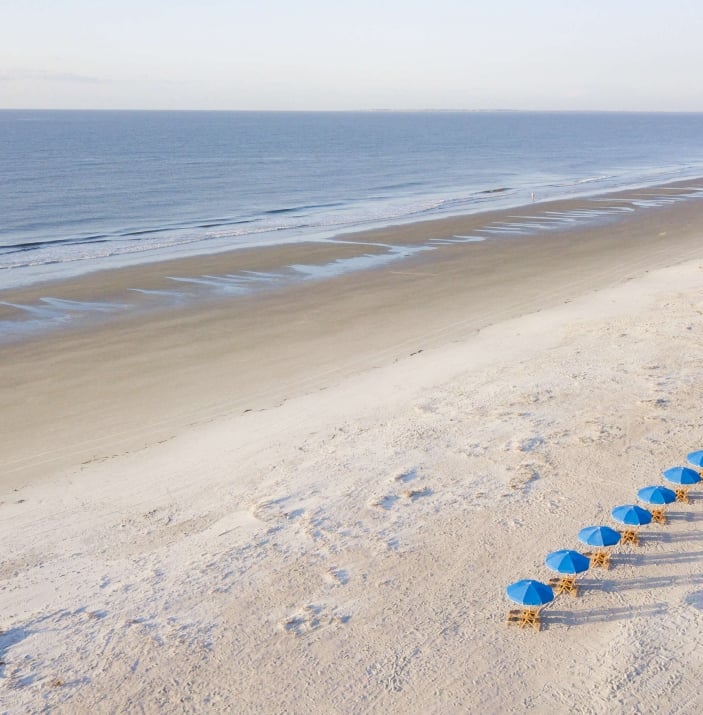 chairs with blue umbrellas lined up on a white sand beach