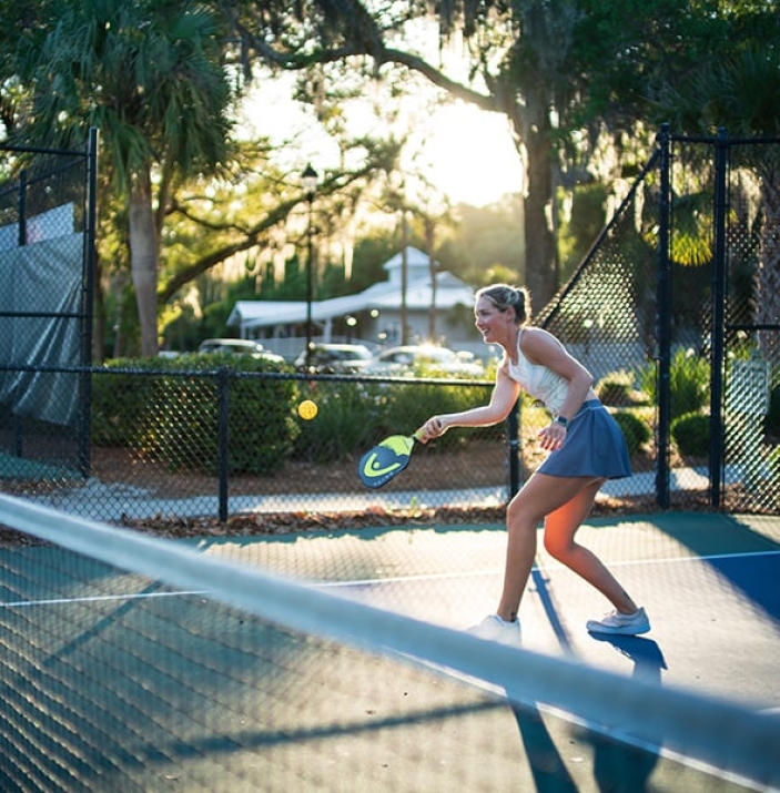 woman playing pickleball at Palmetto Dunes Pickleball Center with sun shining between trees