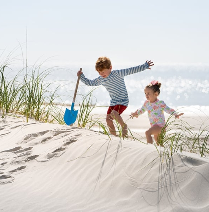 Little boy with shovel and little girl climb the sand dunes at the beach at Palmetto Dunes